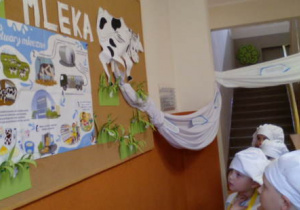 Dzieci w strojach kucharzy podczas rozmowy i oglądania plakatu na wystawie.